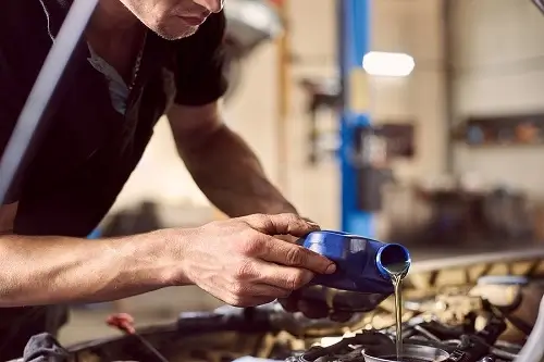 Why Choose Full-Service Auto Repair Shop Over Quick Lube For Oil Change | Kanuga Tire & Auto in Hendersonville, NC. Image of a mechanic pouring oil into a car engine.