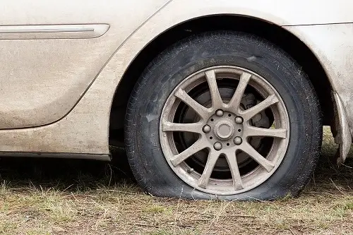 So Many Tire Services—Which One Do I Need? | Kanuga Tire & Auto in Hendersonville, NC. Image of a flat tire on a white car on grass waiting tire repair.