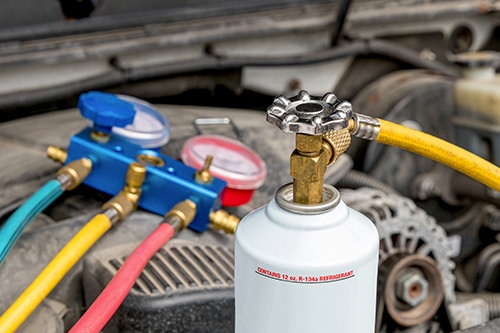 Freon can and test gauges under hood of car. Concept image of “Different Refrigerants for Your Vehicle AC System” | Kanuga Tire & Auto in Hendersonville, NC.