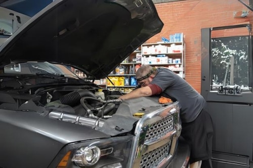 Expert auto repair services in Hendersonville, NC with Kanuga Tire & Auto. Image of mechanic performing auto repair on gray dodge truck at the shop.